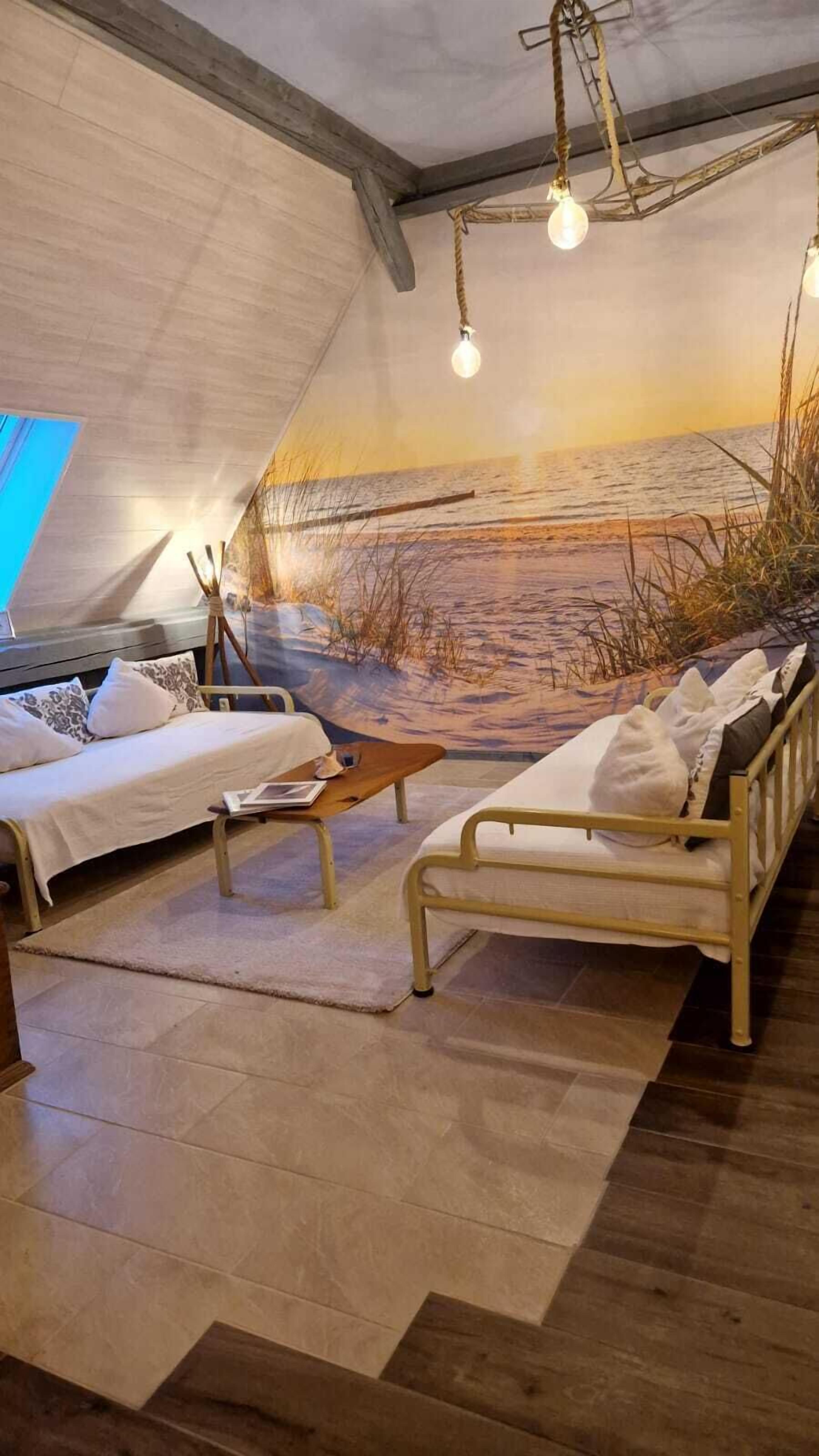 Habitació acollidora amb dos llits, una taula de fusta i un mural d'una platja.