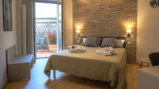 A hotel room with a bed, a small table, a chair, and a view of the outdoors through a glass door. - Little Rock (Gaeta)