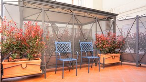 A covered patio area with two blue chairs and two wooden planters with red foliage. - Little Rock (Gaeta)