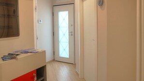 A hallway with a door featuring a geometric glass design, a red and white cabinet with magazines, and a wall-mounted sign. - Little Rock (Gaeta)