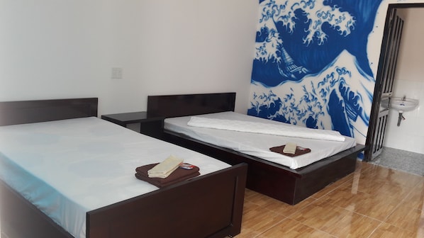 A hotel room with two single beds, a small table, and a wall with a blue and white wave pattern. - Sweethome - Hostel (Bac Nha Trang)