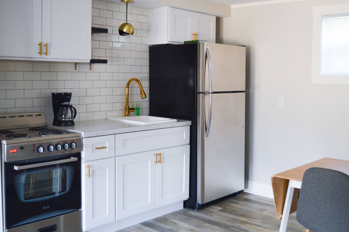 A kitchen with white cabinets, a stainless steel refrigerator, a gas stove, and a coffee maker.
