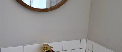 A bathroom with a white sink, gold faucet, and a round mirror with a wooden frame.