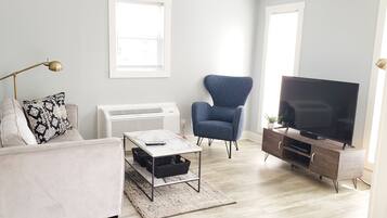 Uma sala de estar moderna com sofá, poltrona, mesa de centro, rack para TV e aparelho de ar condicionado.