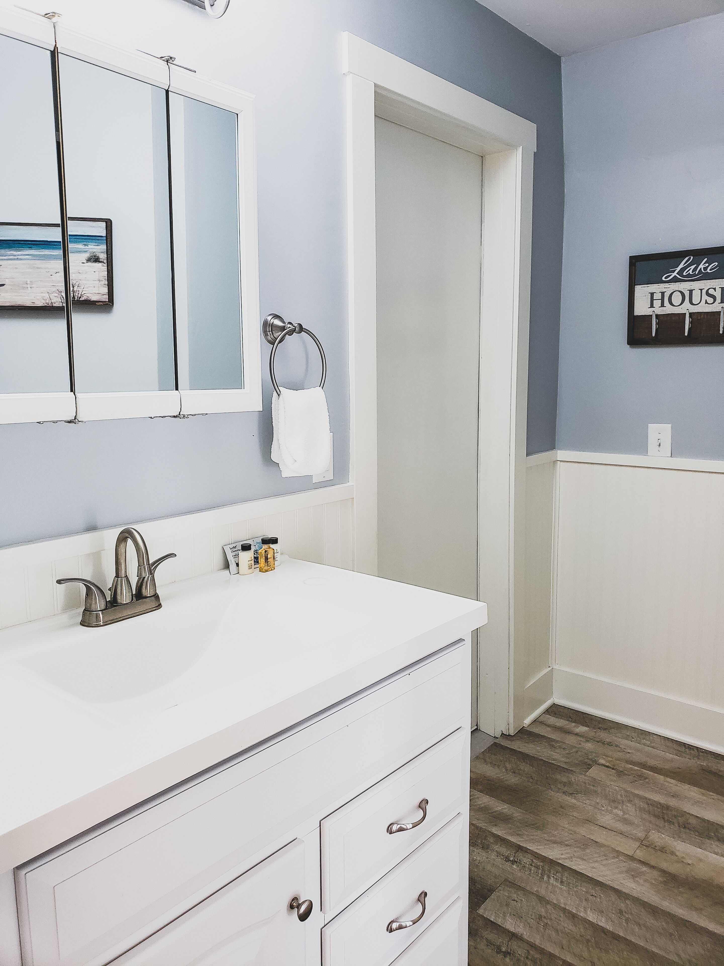 A bathroom with a white vanity, a mirror, a towel ring, and a sign on the wall.