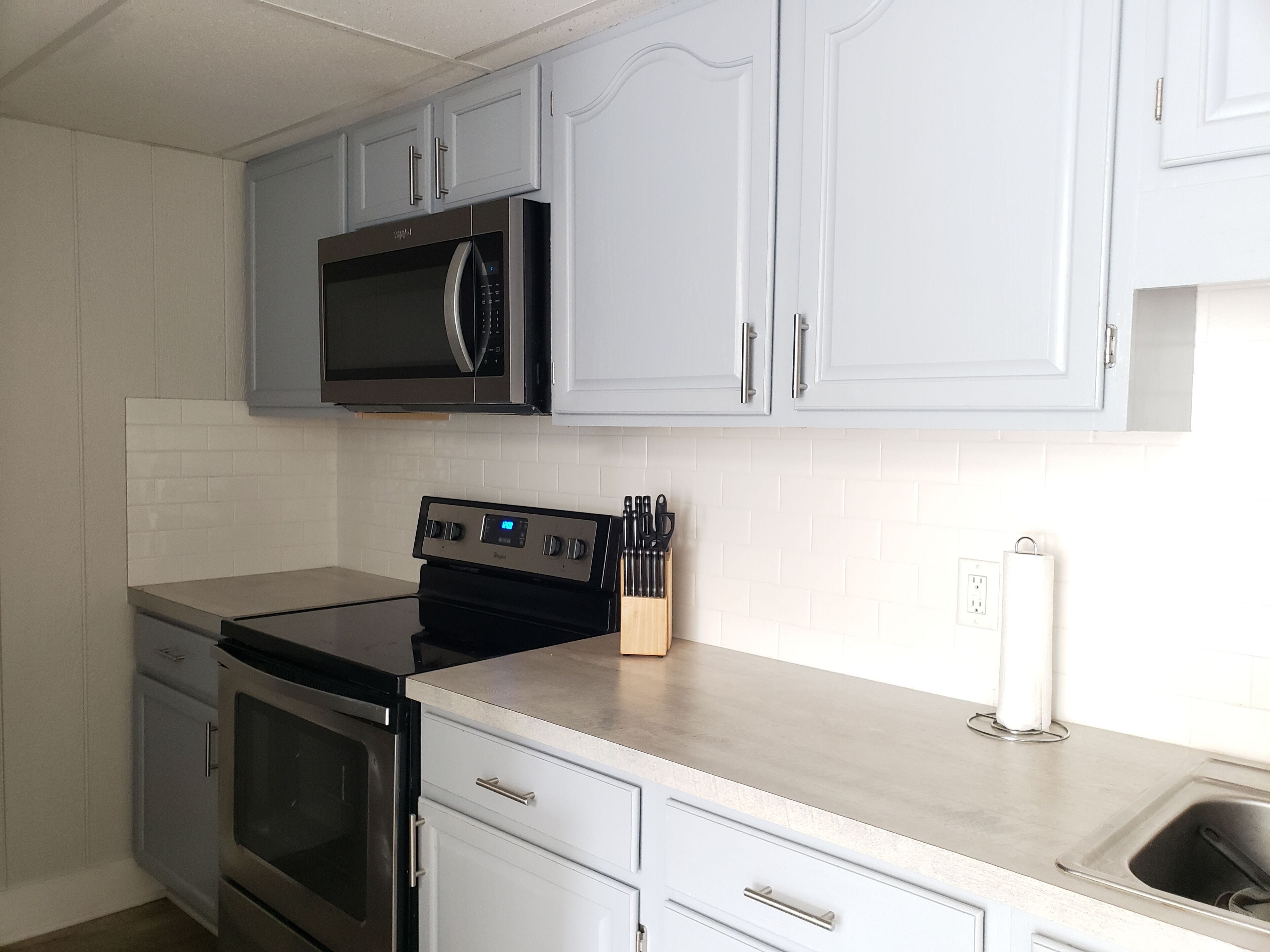 A kitchen with white cabinets, a stainless steel microwave, a gas stove, and a sink.
