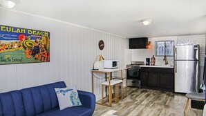 Uma cozinha compacta com micro-ondas, forno e frigorífico. Um sofá azul e uma pequena mesa estão na sala de estar.