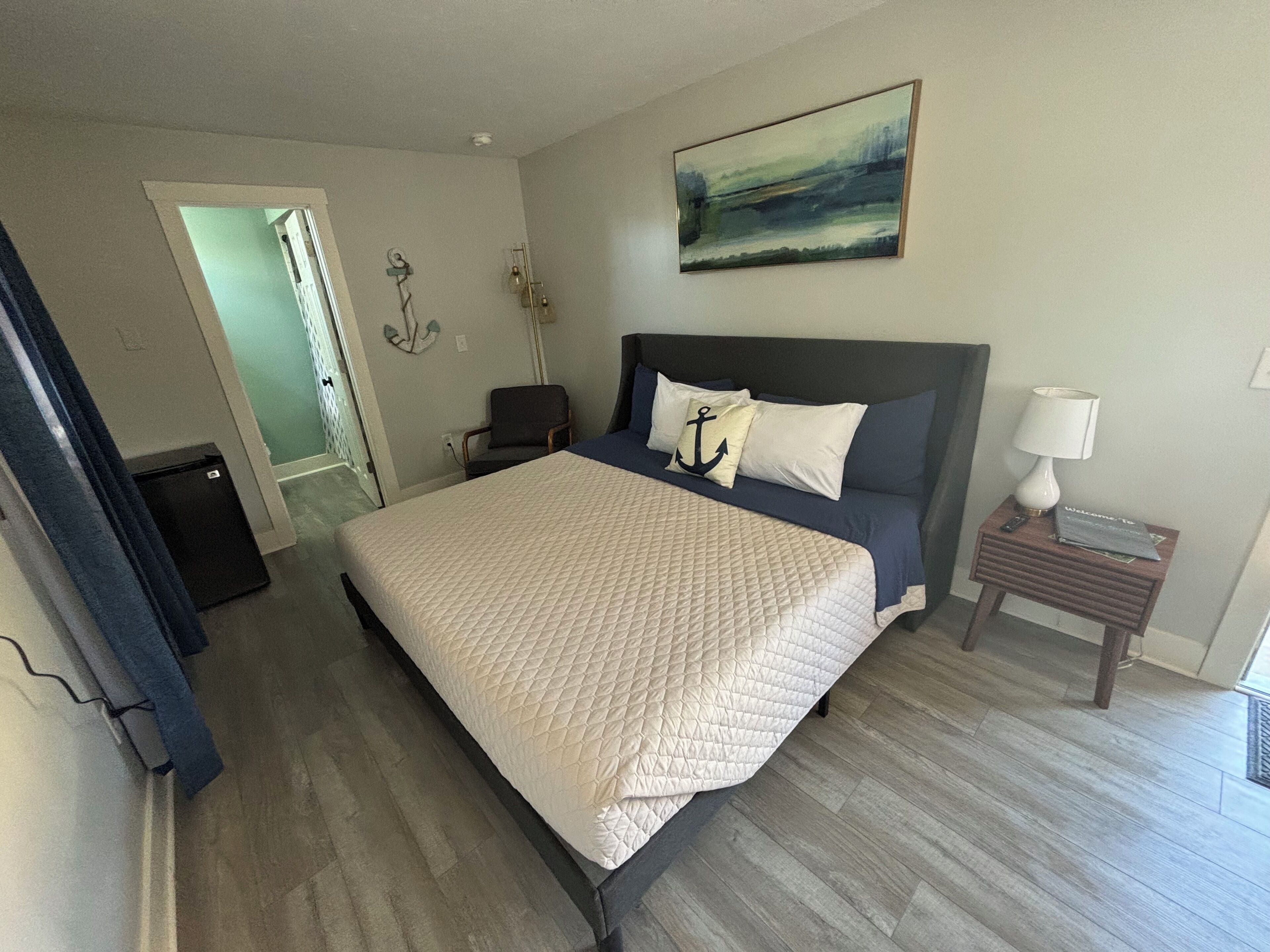 A hotel room with a bed, a nightstand, a chair, a desk, and a painting on the wall.