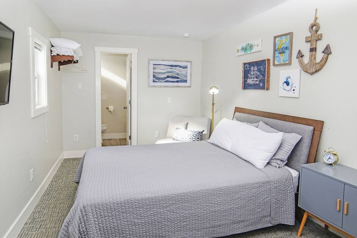 A neatly arranged bedroom with a bed, bedside table, and wall decorations including a framed anchor and artwork.