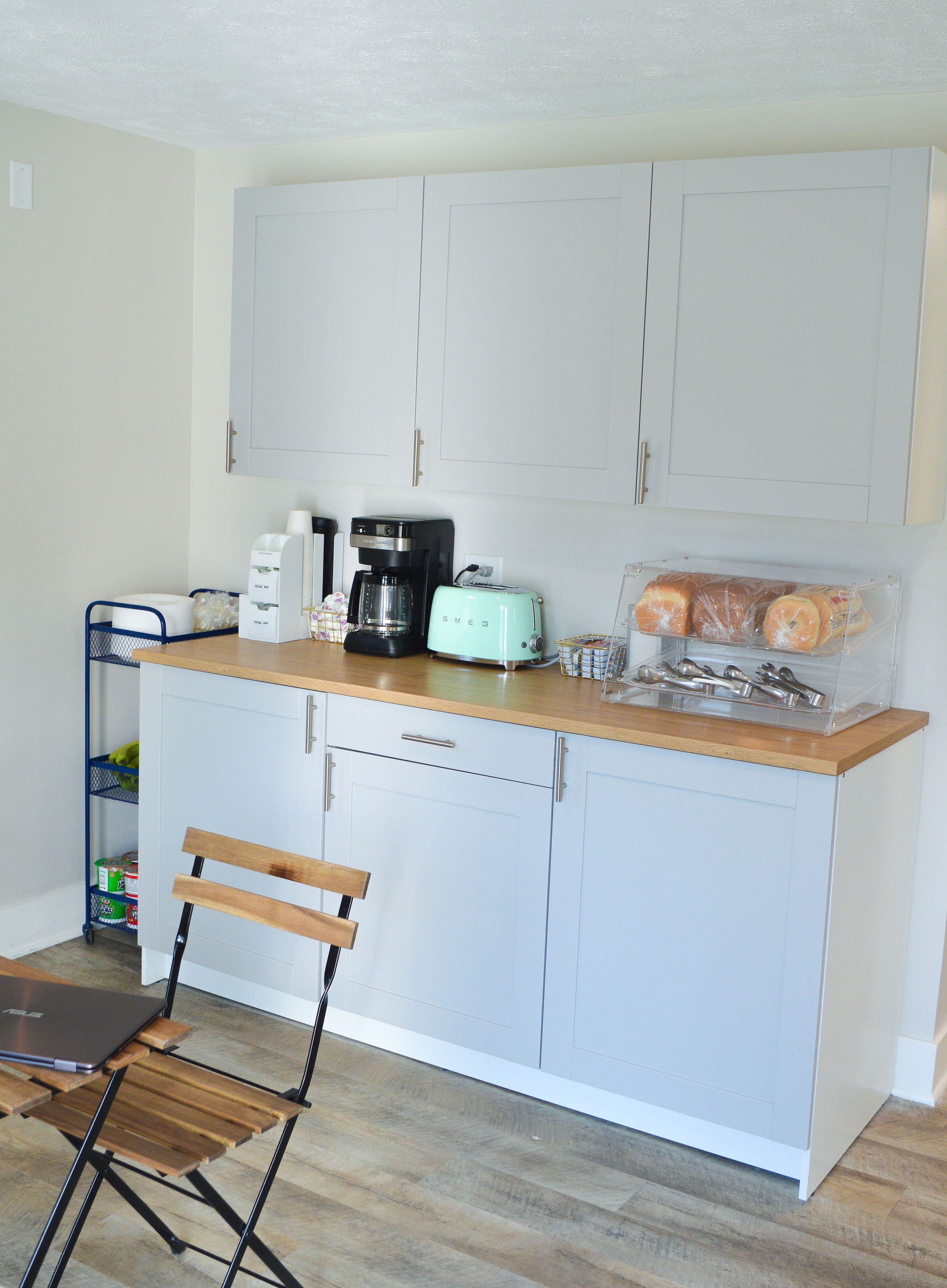 A compact kitchen with white cabinets, a coffee maker, a toaster, and a bread box.