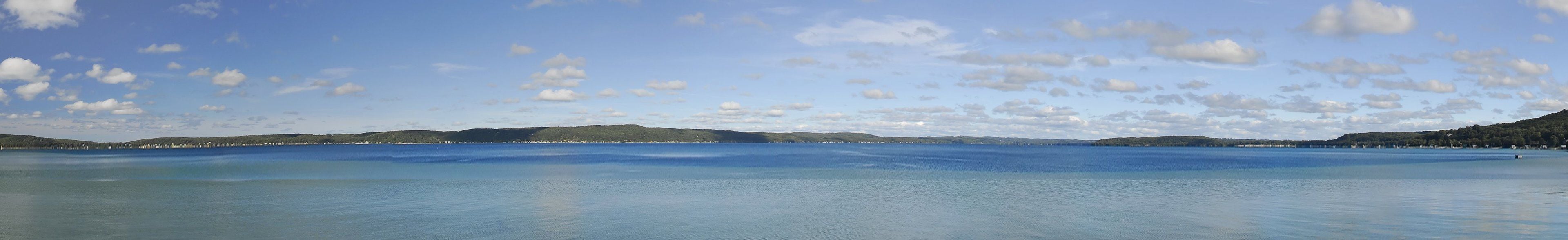 Een panoramisch uitzicht op een kalm meer, met heuvels in de verte en een heldere lucht.