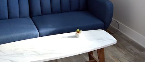 A blue sofa, a white marble coffee table, and a gold floor lamp in a room with wooden flooring.