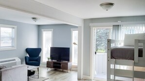Quarto com televisão, uma cadeira azul, cama e aquecedor branco.