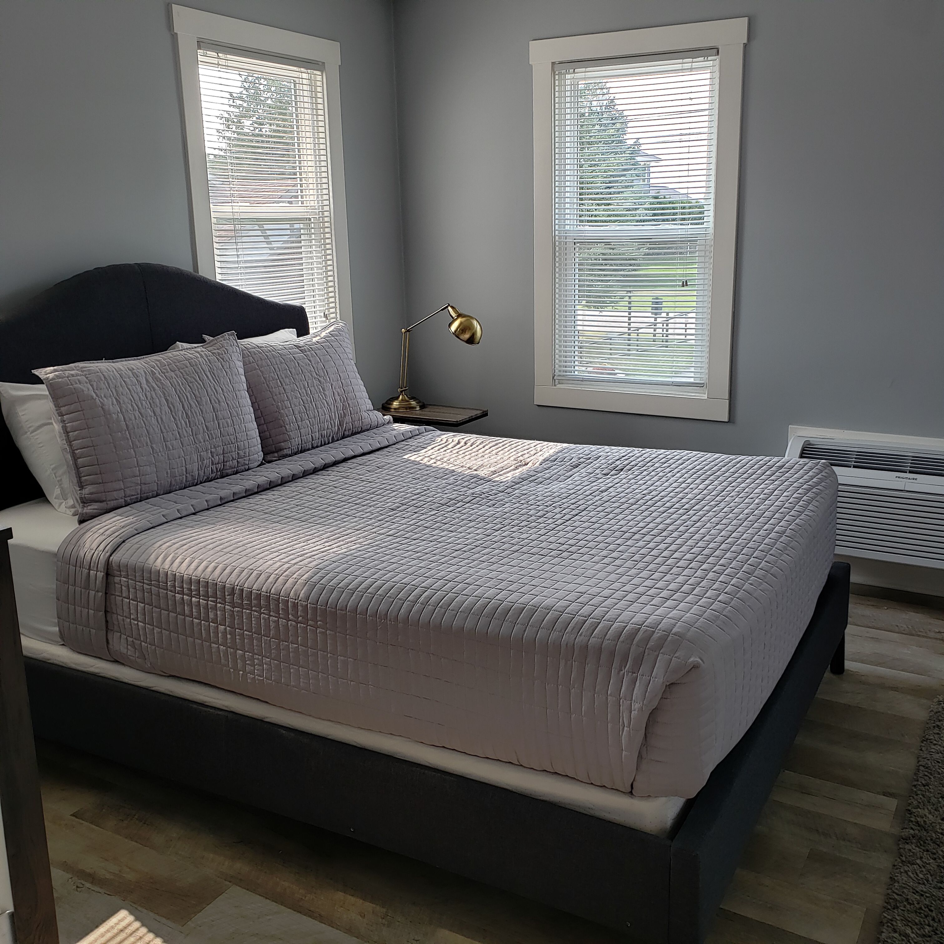 Un dormitorio con cama, mesita de noche, lámpara y aire acondicionado.