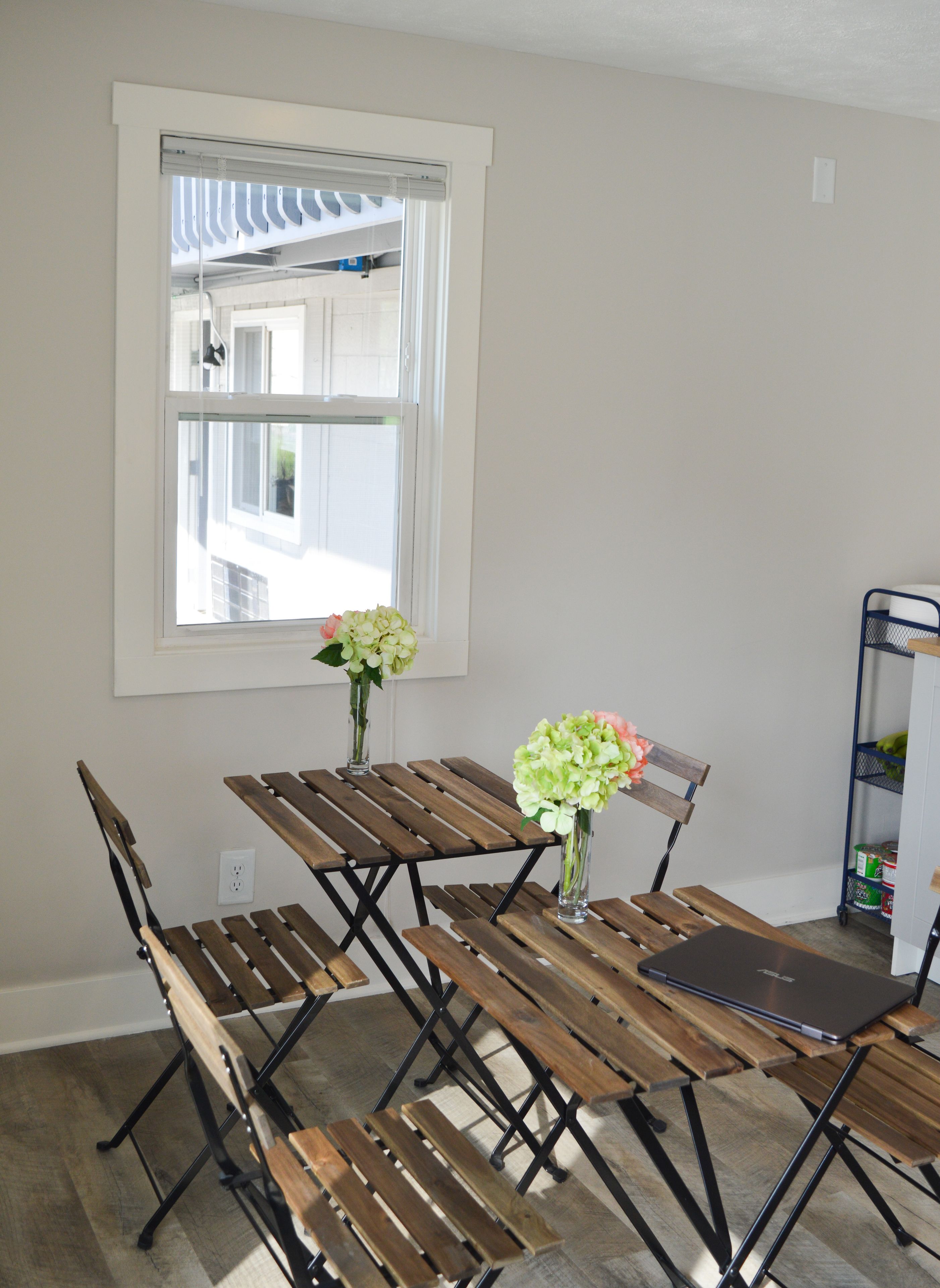 Un comedor con mesa de madera y bancos, una ventana con persianas y un ordenador portátil sobre la mesa.