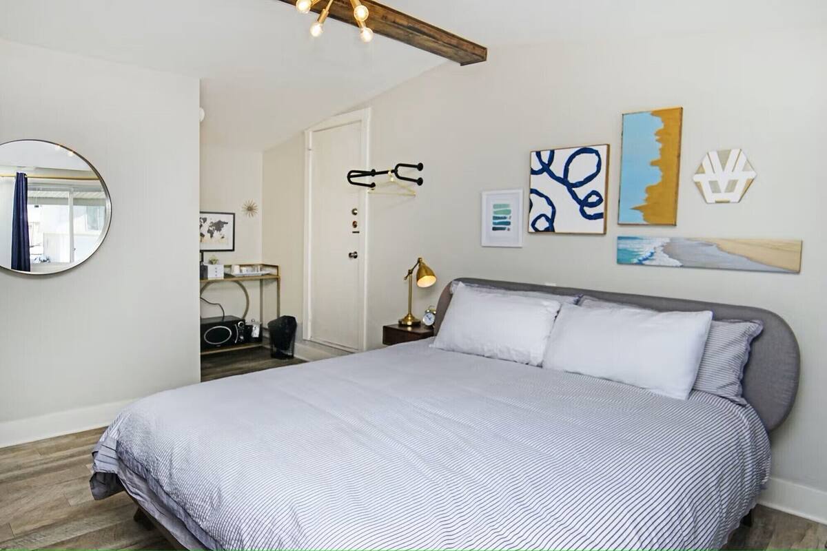 A bedroom with a large bed, a round mirror, and artwork on the walls.