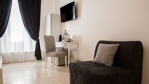 A room with a dark upholstered sofa, a white desk with a mirror, and a television mounted on the wall. - Lifestyle Veneto Suite (Rome)