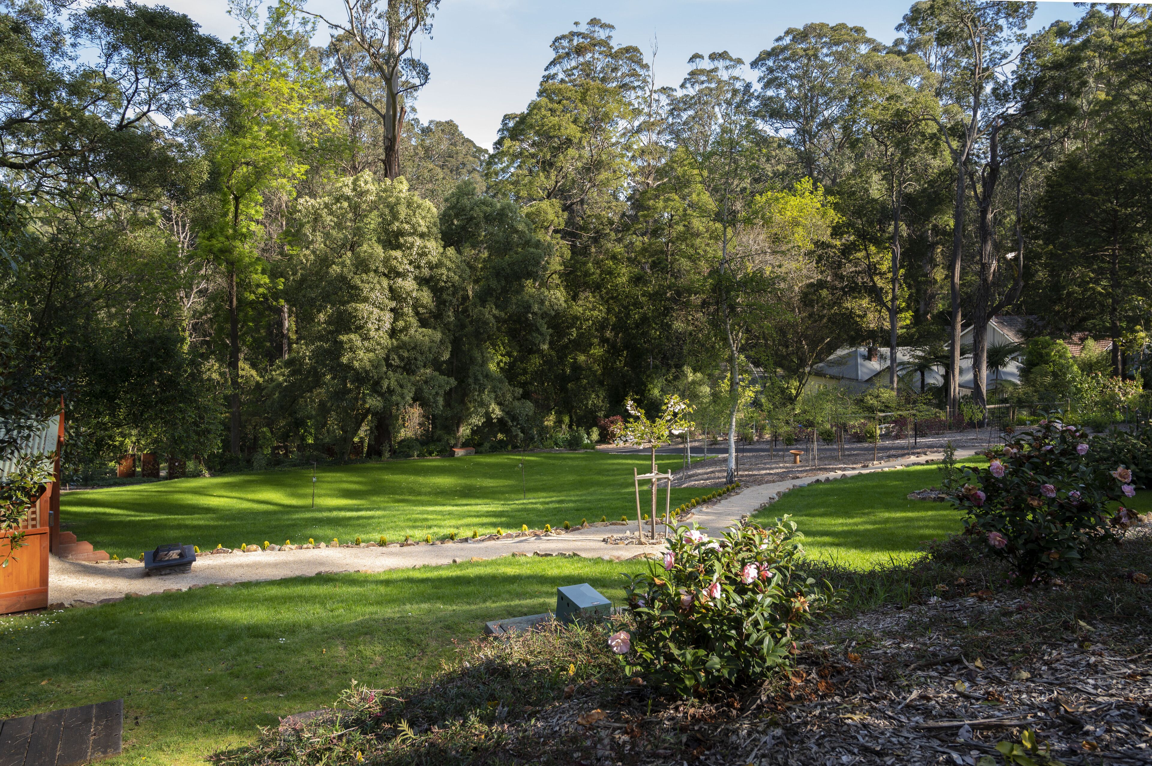 A well-maintained garden with a lawn, pathway, and a variety of trees.