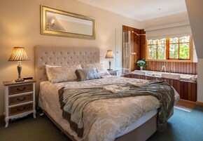 Ein Schlafzimmer mit einem großen Bett, zwei Nachttischen, einem Spiegel, einem Fenster mit Aussicht und einem Badezimmer mit Waschbecken und Spiegel.