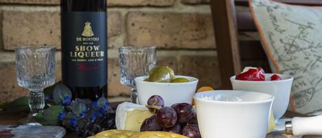 A table with a bottle of wine, glasses, cheese, grapes, crackers, and a cutting board.