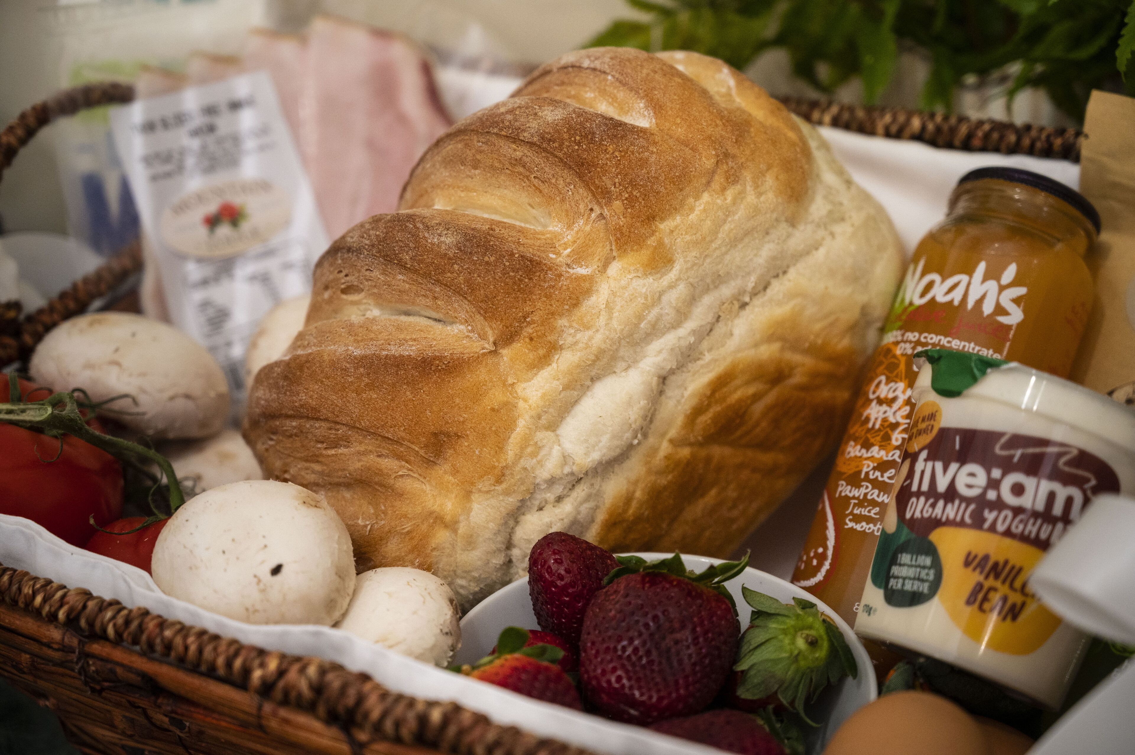 A basket containing bread, strawberries, eggs, and a jar of organic yogurt.