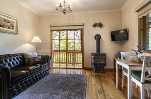 Ein Wohnzimmer mit einer schwarzen Ledersofa, einem Holztisch, einem Kamin, einem Fernseher und einem großen Fenster mit Blick auf Bäume.