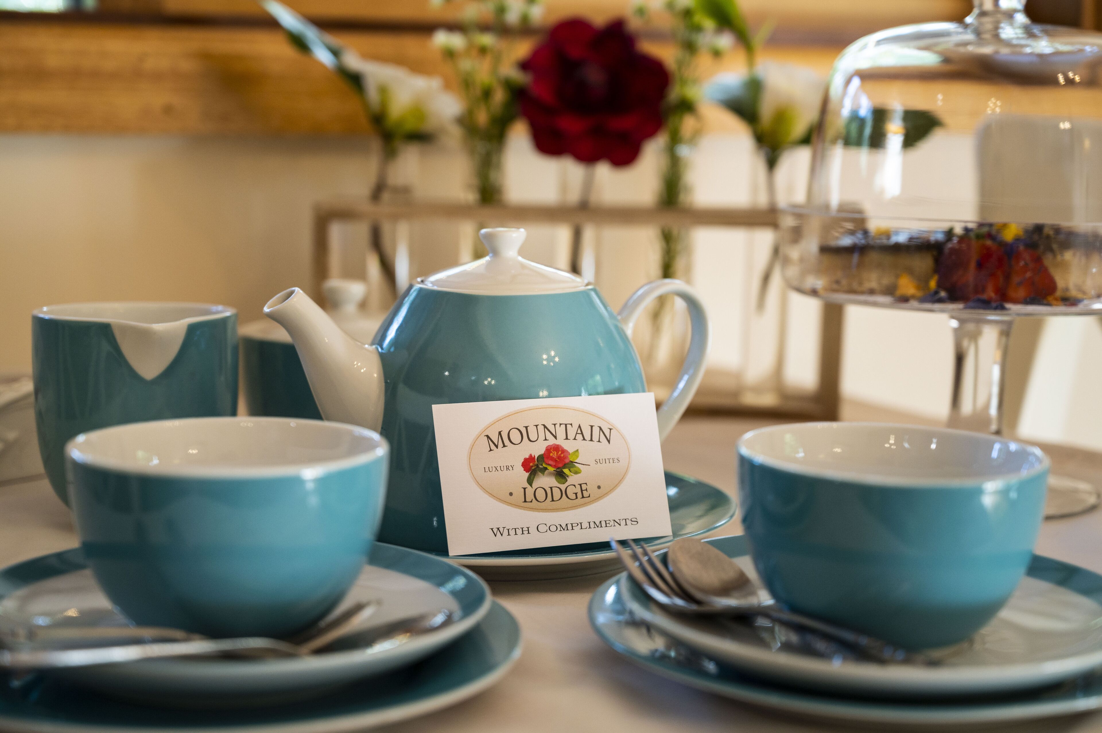 A tea set with a teapot and cups on a table, accompanied by a sign that reads "Mountain Lodge With Compliments".