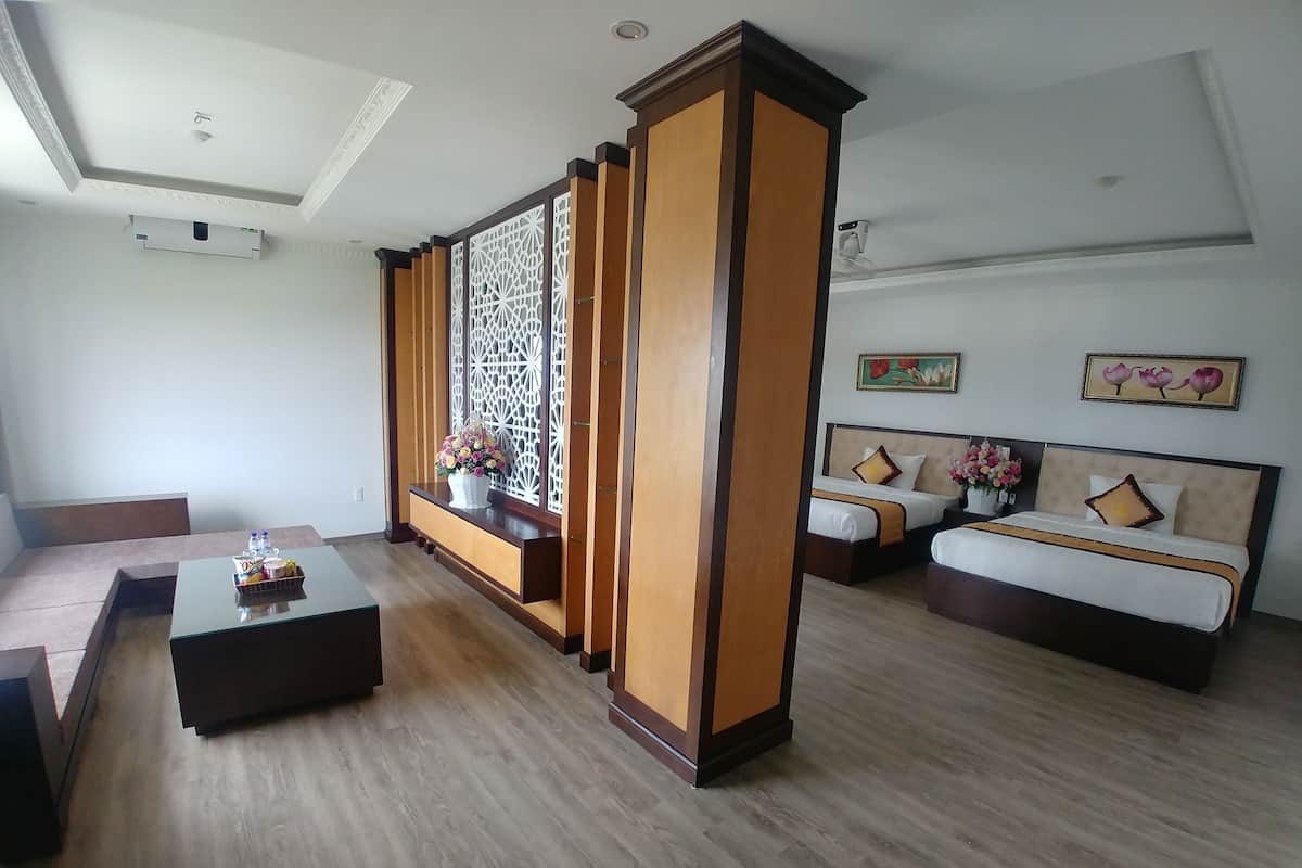 A modern hotel room with a wooden floor, a sofa, a coffee table, a bed with a headboard, and a decorative partition.