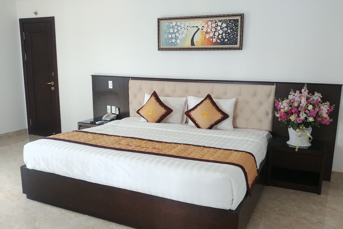 A hotel room with a large bed, a nightstand with a phone, a wall-mounted painting, and a vase of flowers.