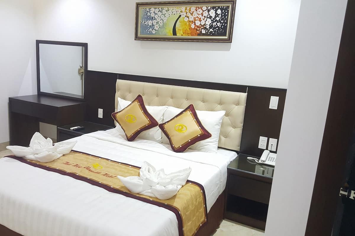 A hotel room with a bed, a bedside table, a nightstand, a mirror, and a painting on the wall.