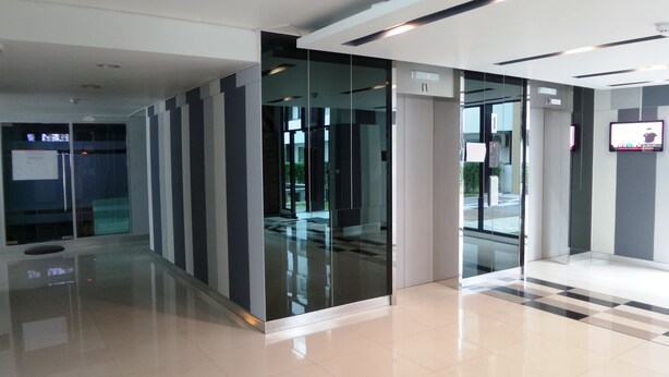 A modern lobby with glass doors, a checkered floor, and a digital display on the wall. - PLUM Condo Phaholyothin 89 (Thanyaburi)