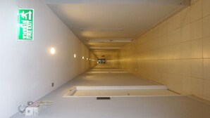 A corridor with a green fire exit sign, tiled walls, and a ceiling with recessed lighting. - PLUM Condo Phaholyothin 89 (Thanyaburi)