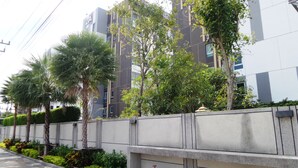 A modern building with a concrete facade, surrounded by well-maintained greenery and palm trees. - PLUM Condo Phaholyothin 89 (Thanyaburi)