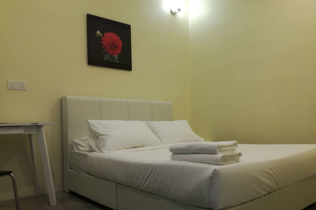 A neatly made bed with white linens, a small bedside table, and a wall-mounted light fixture.