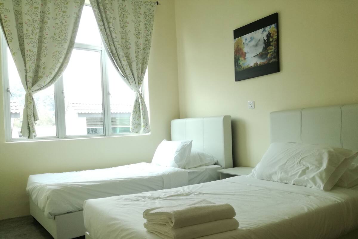 A hotel room with two beds, a window with curtains, a painting on the wall, and a view of buildings outside.