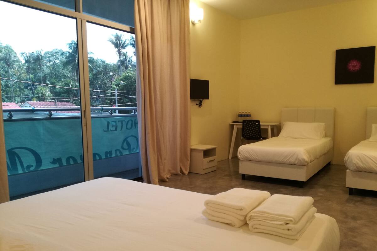 A hotel room with two beds, a desk, a chair, and a window with a view of palm trees.