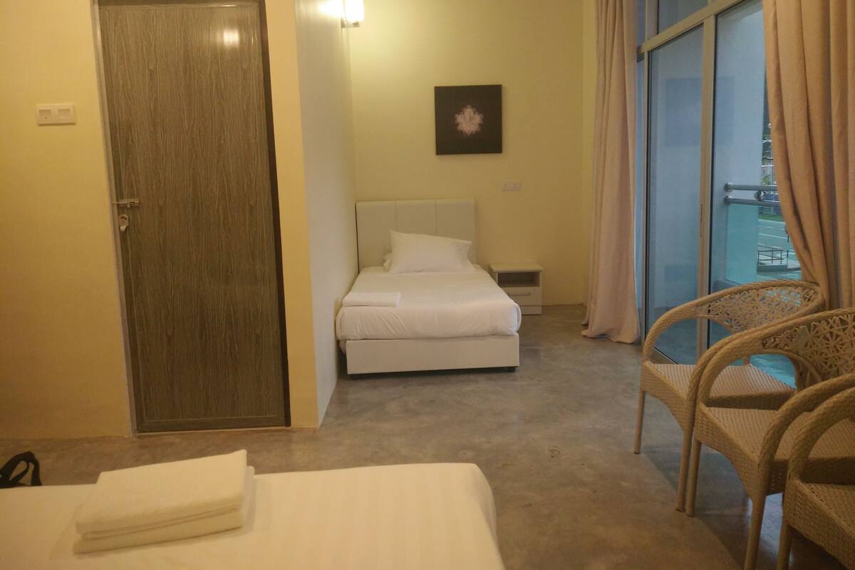 A hotel room with a bed, a chair, a door, and a window with curtains.