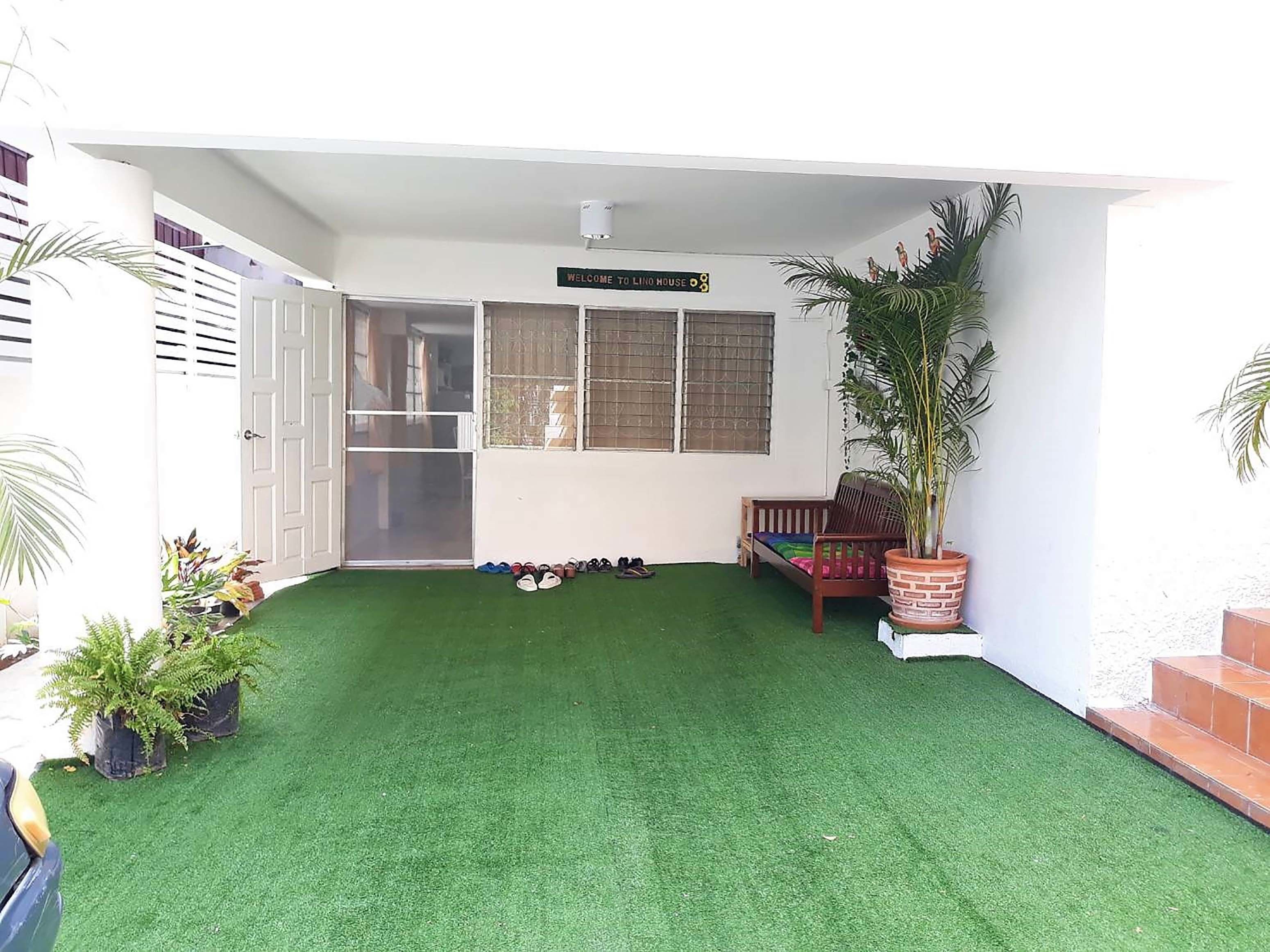 A covered patio area with artificial grass, a wooden bench, a potted plant, and a sign reading "WELCOME TO LINO HOUSE."