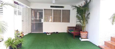 A covered patio area with artificial grass, a wooden bench, a potted plant, and a sign reading "WELCOME TO LINO HOUSE."
