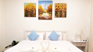 Ein Hotelzimmer mit einem ordentlich bezogenen Bett, einem Nachttisch mit Lampe und drei Baumdarstellungen an der Wand.