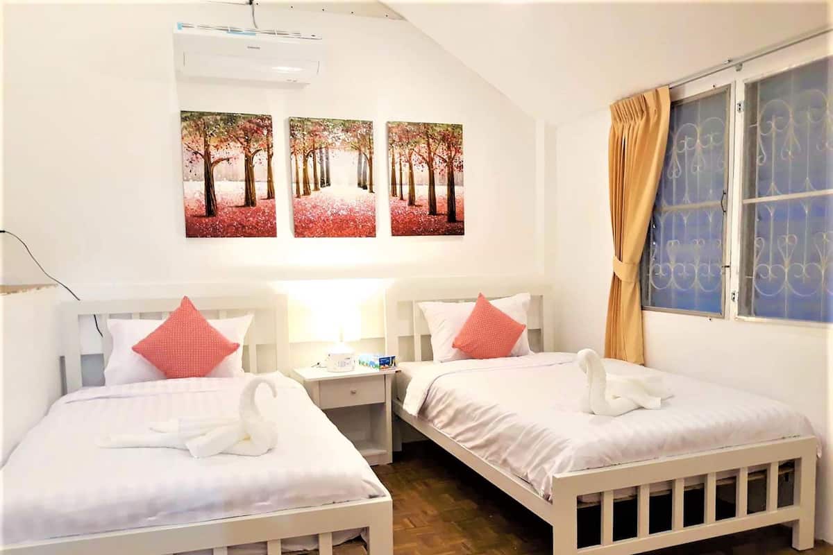 A room with two beds, each with white bedding and red pillows, a nightstand with a lamp, and three framed pictures on the wall.