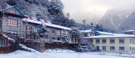 Un edificio tradicional con techo inclinado y varias ventanas, rodeado de árboles nevados y montañas.