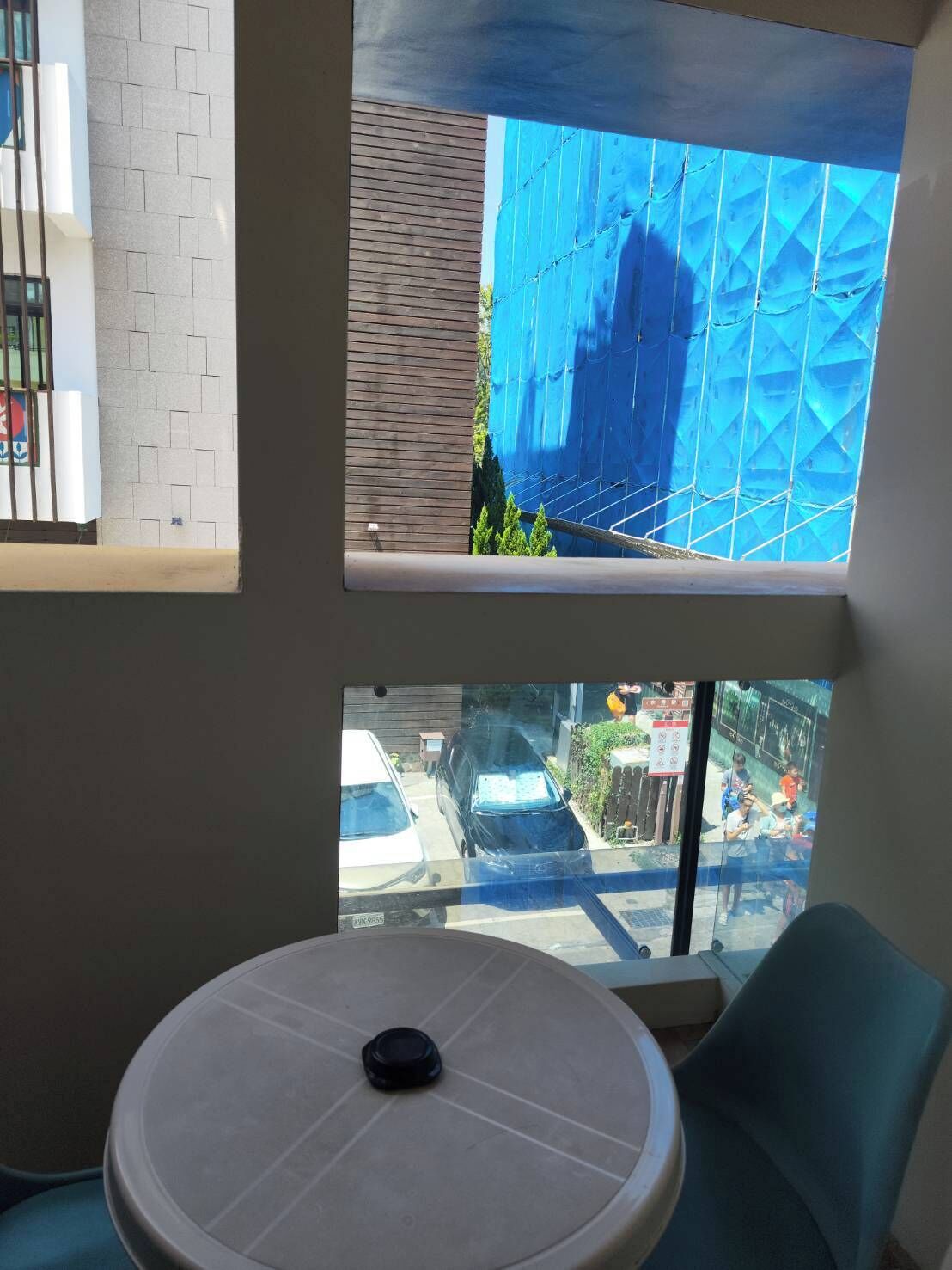 Une pièce avec une table ronde et une chaise, une fenêtre donnant sur un immeuble bleu et une rue animée.