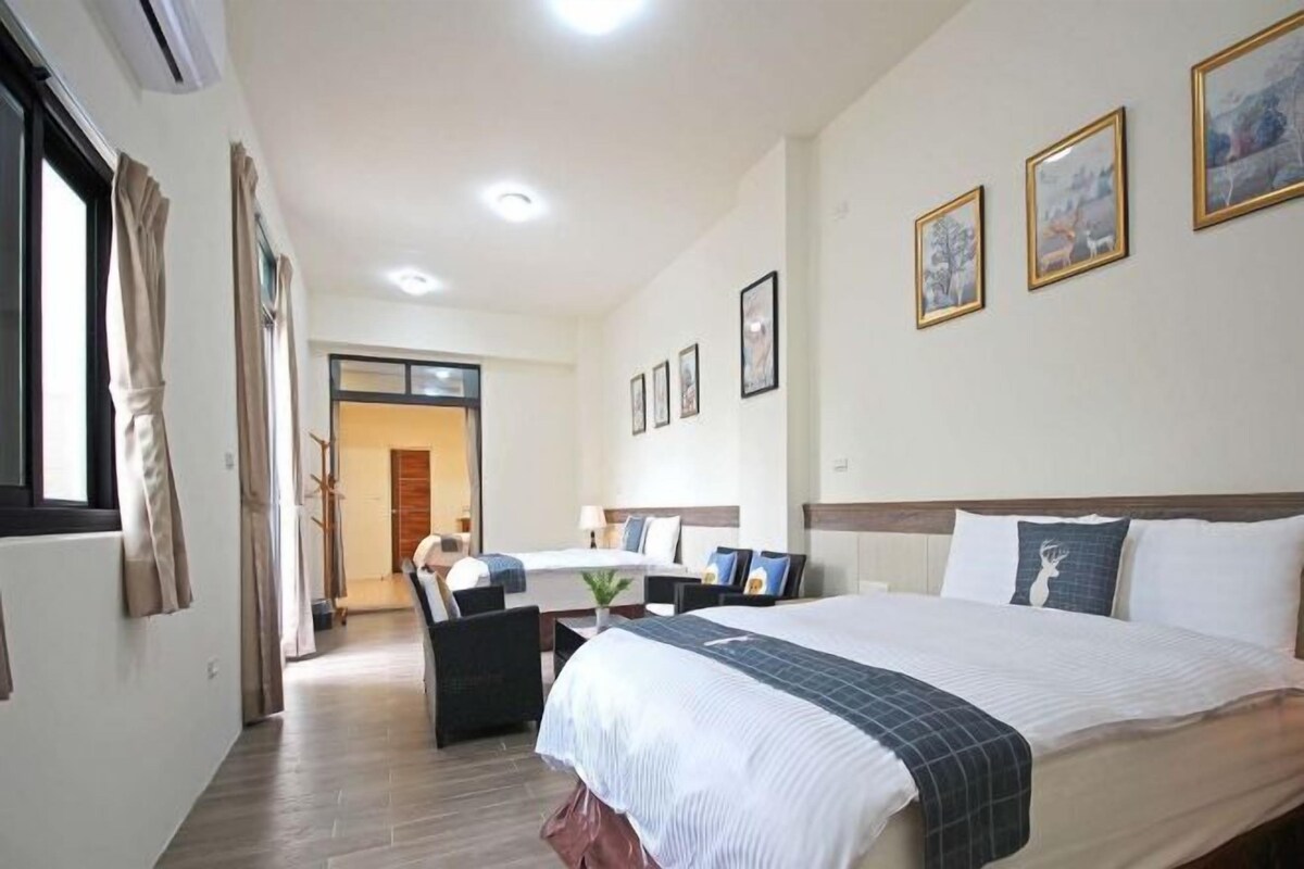 A hotel room with a large bed, a desk, and a chair. There are three framed pictures on the wall.