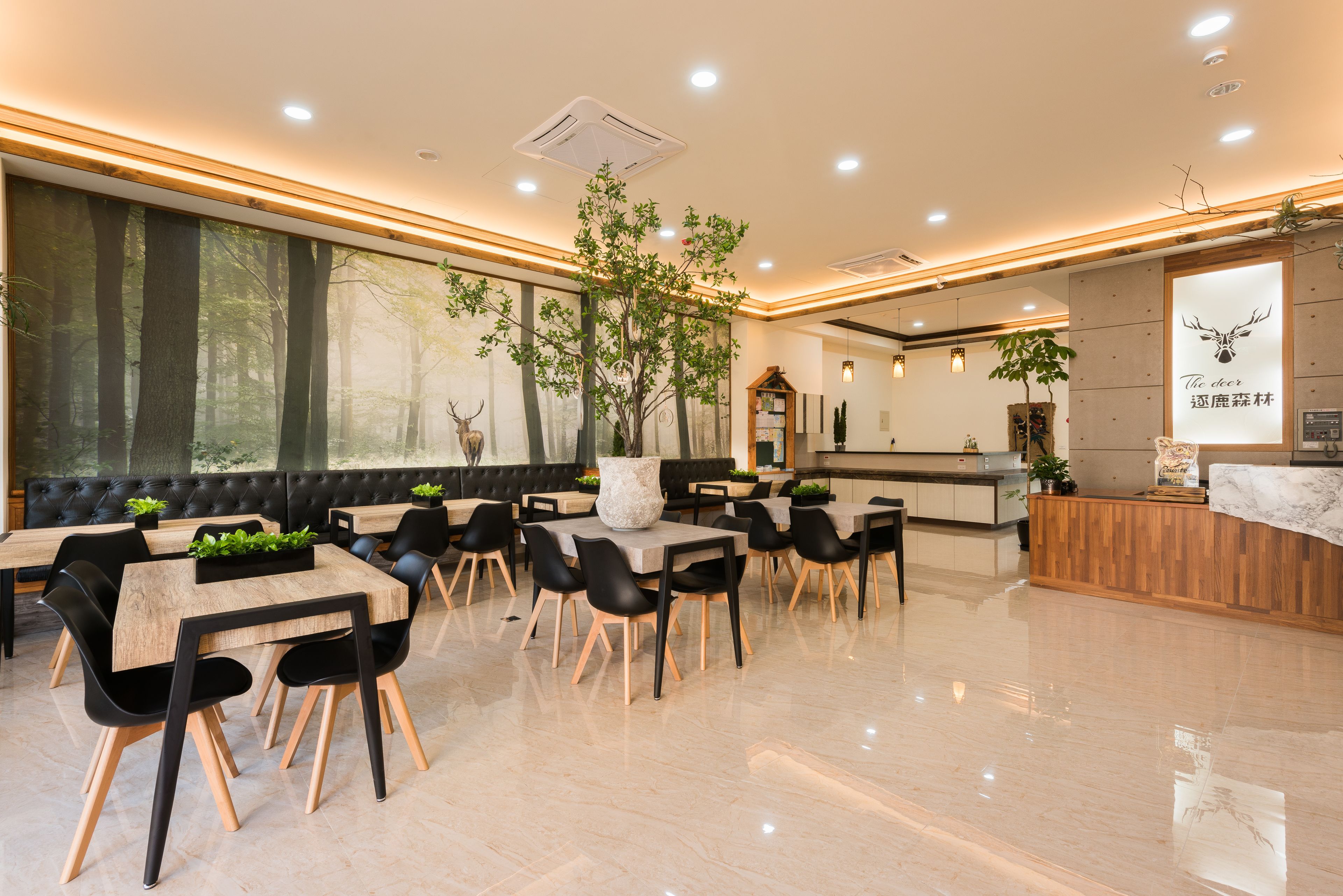 A modern dining area with wooden tables and black chairs, large windows with a forest view, and a reception desk with a deer sign.