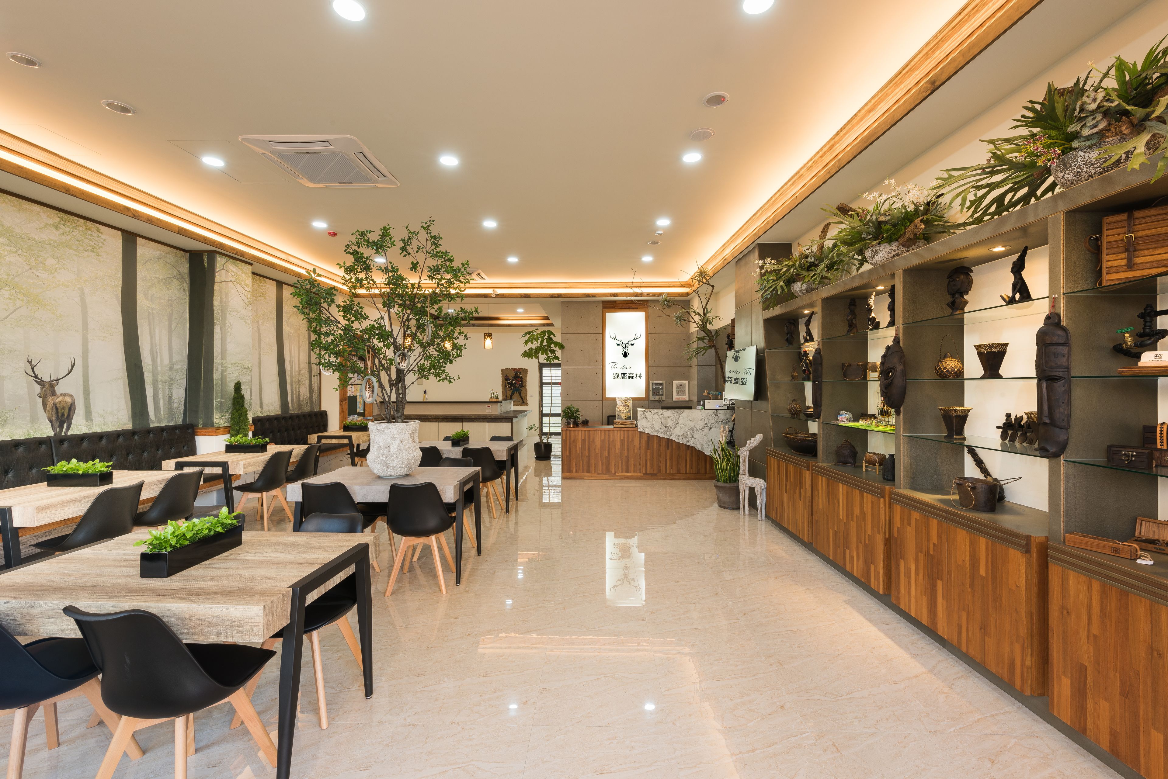 Un amplio vestíbulo de hotel con un mostrador de recepción alargado, varias zonas de estar y una variedad de elementos decorativos y plantas.