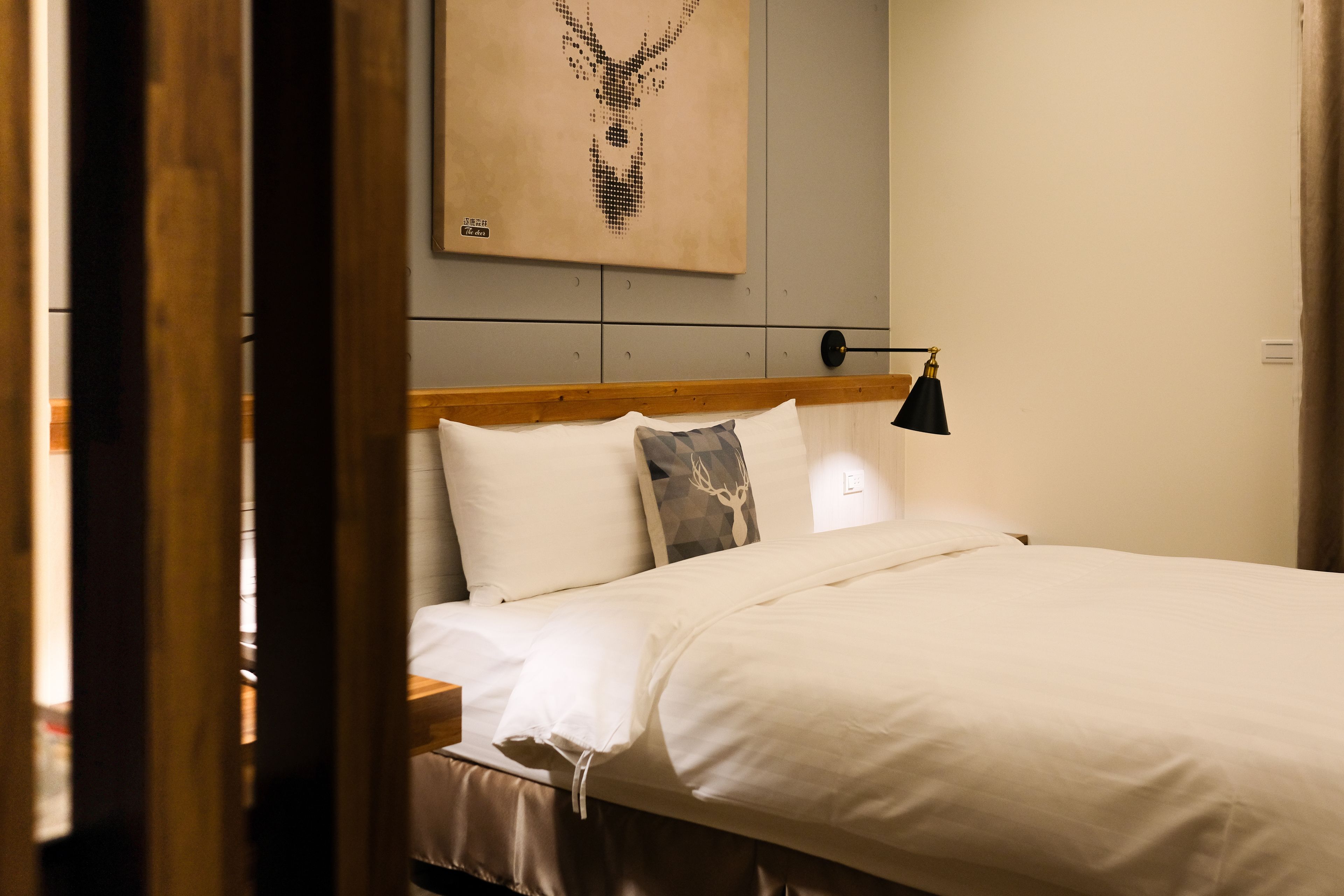 A neatly made bed with white linens, a wooden headboard, and a single black bedside lamp.