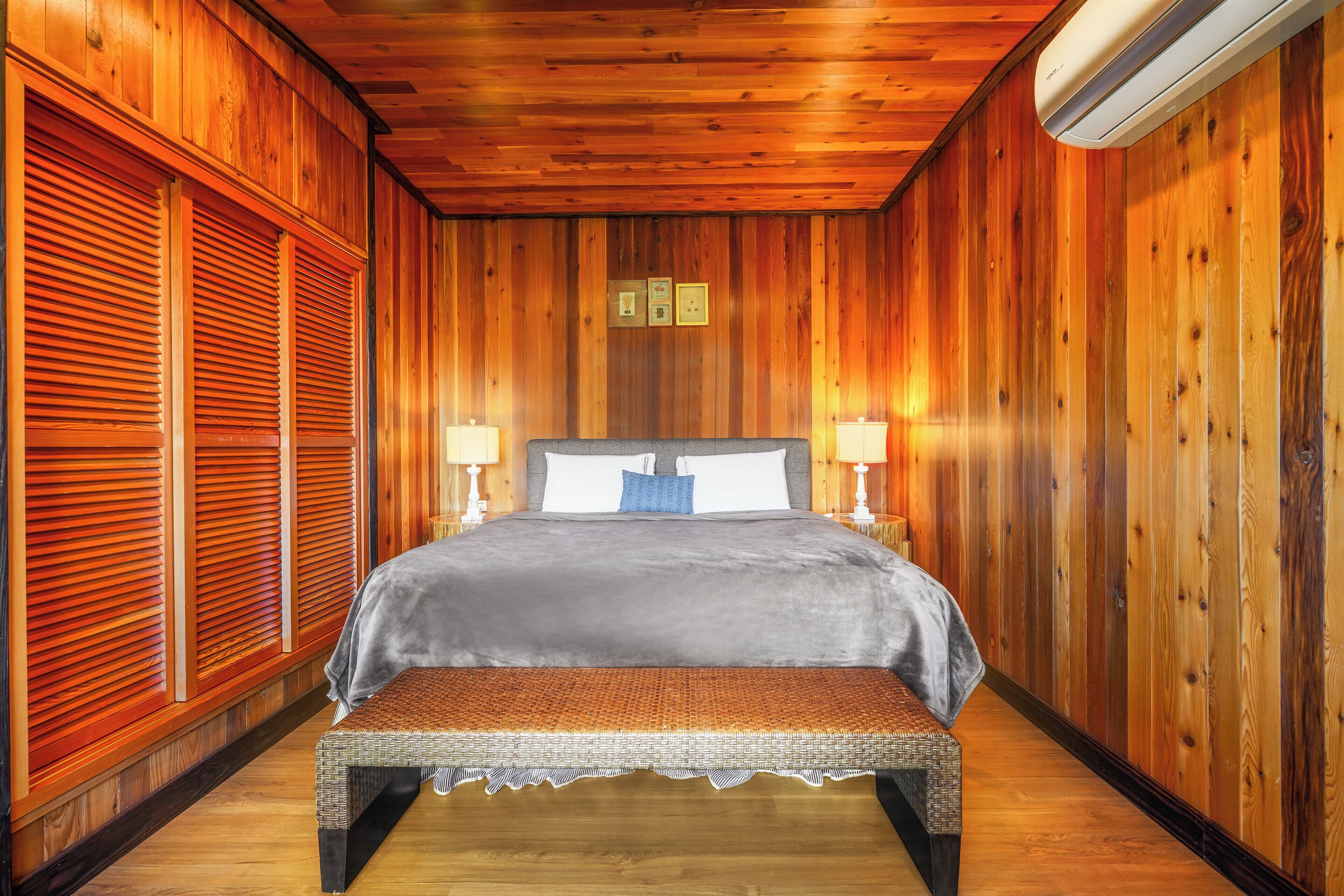 A wooden-paneled room with a bed, two bedside lamps, and a bench.