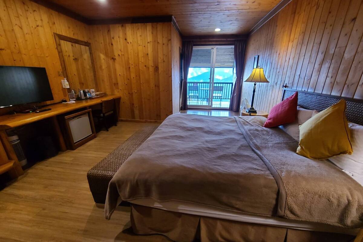 A wooden-paneled bedroom with a bed, a desk, a television, and a view of the outdoors.