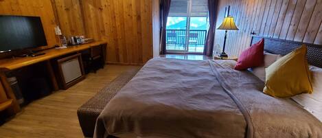 A wooden-paneled bedroom with a bed, a desk, a television, and a view of the outdoors.